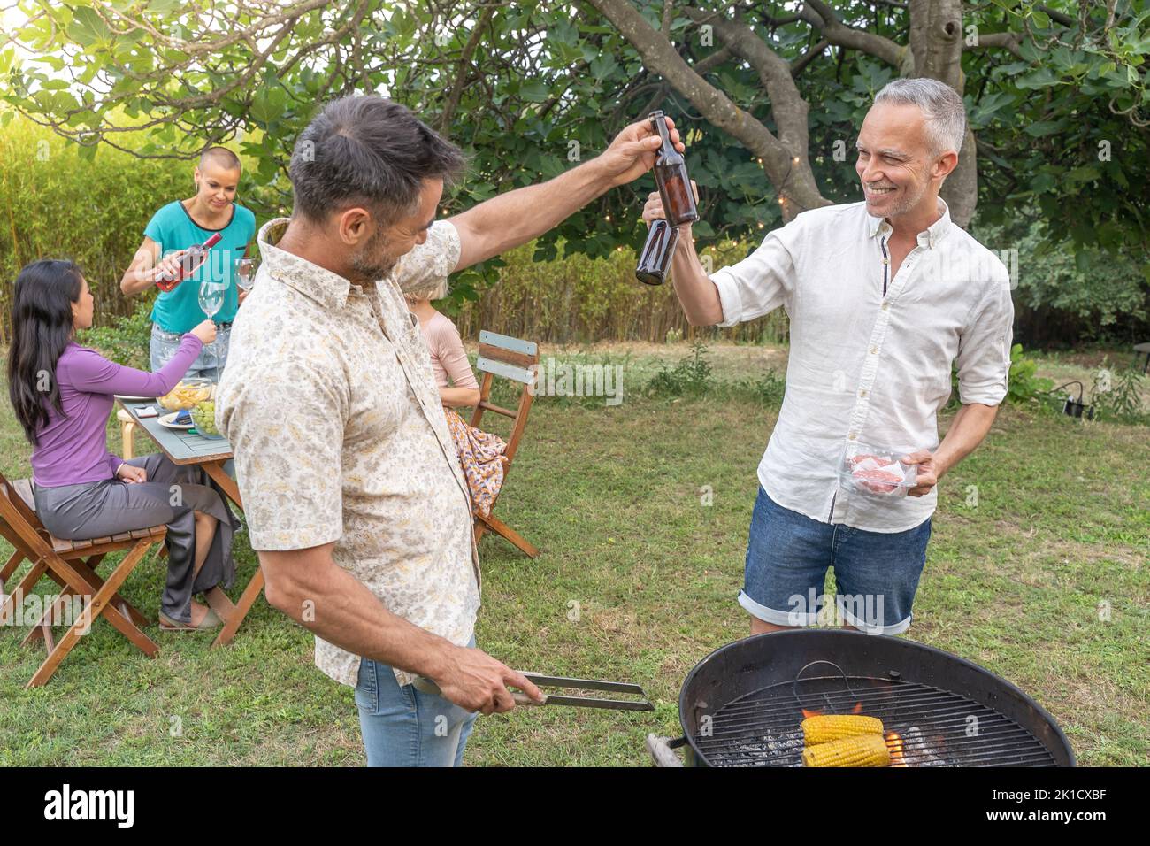 Groupe d'amis qui se sont mis à griller autour du barbecue. Des gens souriants buvant sur le patio. Banque D'Images