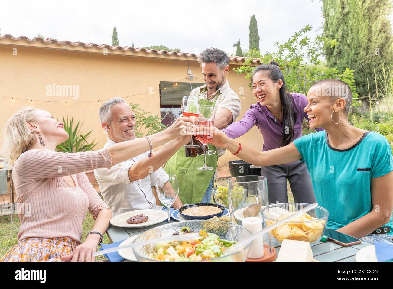 Groupe d'amis matures et gaies qui déguerent un plaisir avec un grand sourire autour de la table au restaurant de la maison sur le patio. Banque D'Images