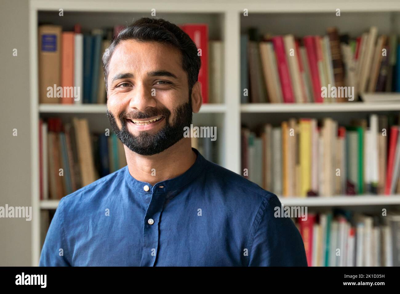Joyeux homme d'affaires indien enseignant debout devant les étagères, portrait. Banque D'Images