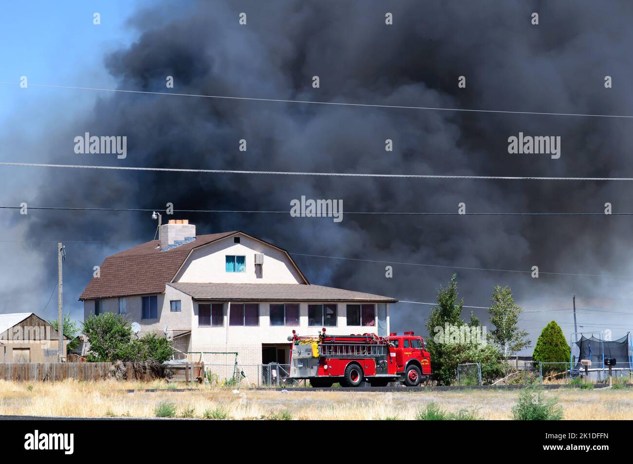 Camion de feu sur la scène d'un feu de maison avec d'énormes nuages de fumée de billing remplissant le ciel. Banque D'Images