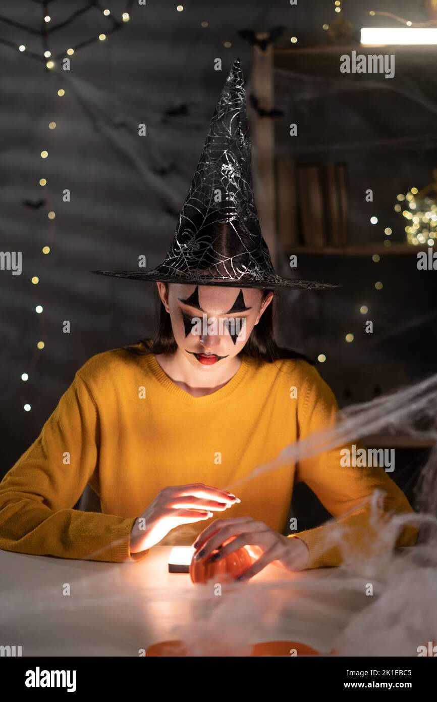 Jeune femme sorcière avec maquillage d'halloween qui se fait sentir à la maison la nuit tenant tfkwu et la lumière dans ses mains, halloween célébration à la maison concept Banque D'Images