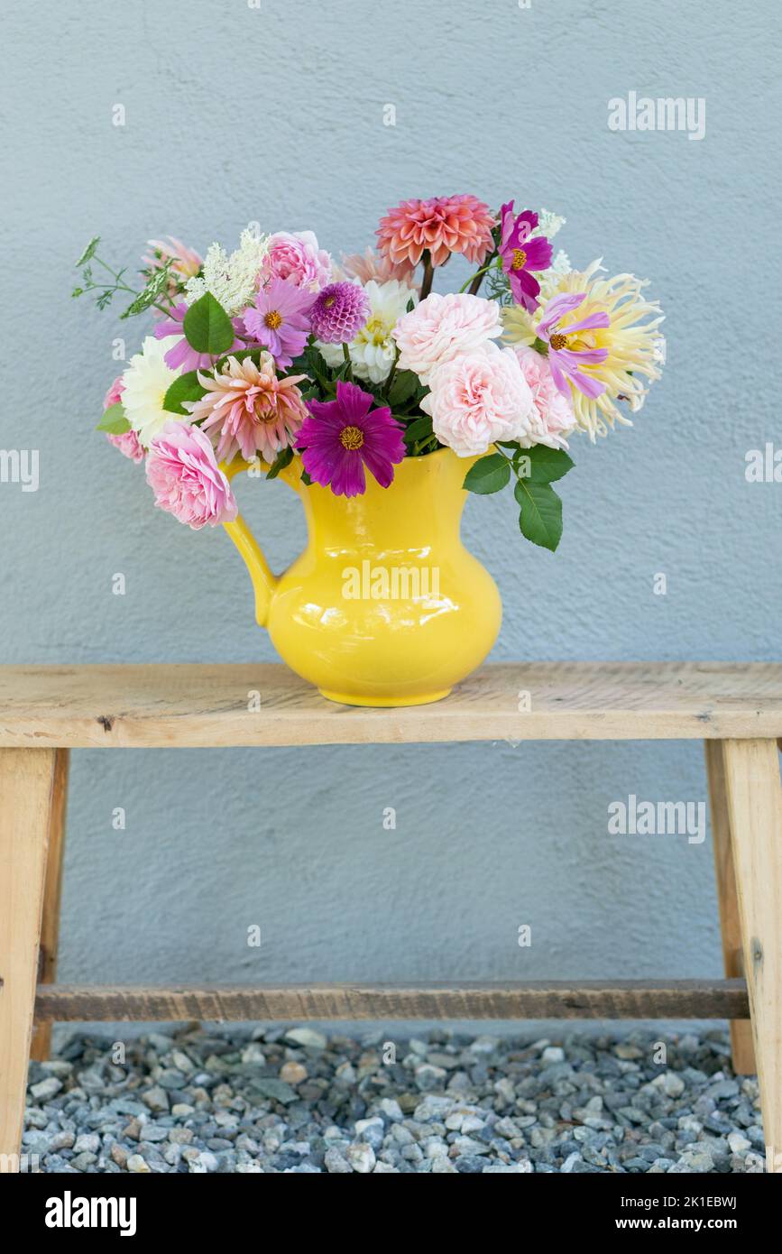 Une photo verticale d'un bouquet floral doux dans un vase jaune sur une table de console en bois Banque D'Images