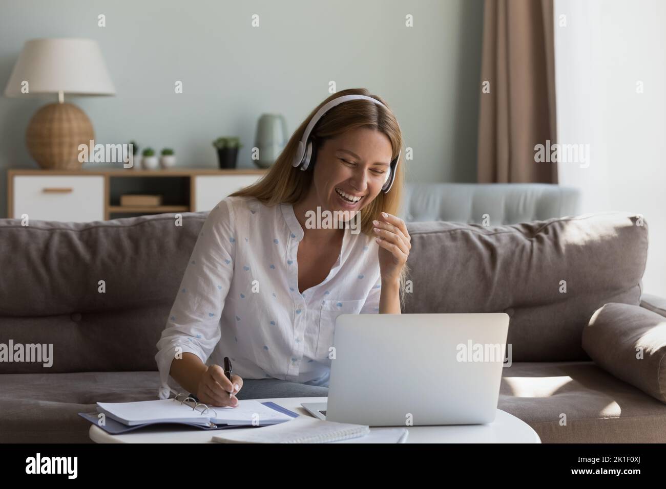 Bonne joyeuse femme dans un casque sans fil parlant lors d'un appel vidéo Banque D'Images