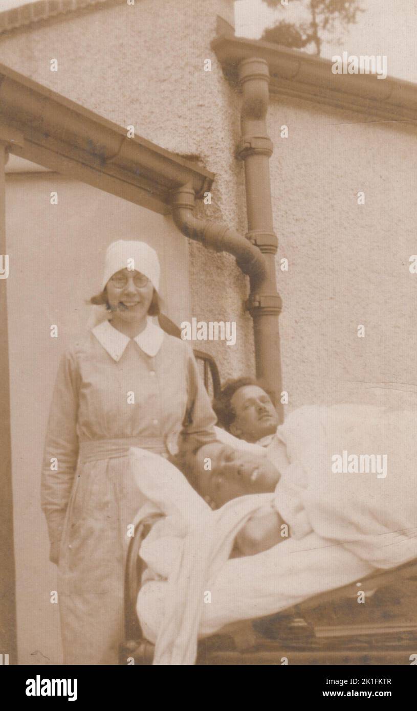 Infirmière et patients, début du 20th siècle. L'infirmière est debout en uniforme, souriante, près des lits d'hôpital qui ont été apportés à l'extérieur. Deux patients masculins sont couchés dans les lits, tous deux orientés vers la caméra. La photographie a été produite par Jerome Ltd., 416 Holloway Road, London N7 Banque D'Images