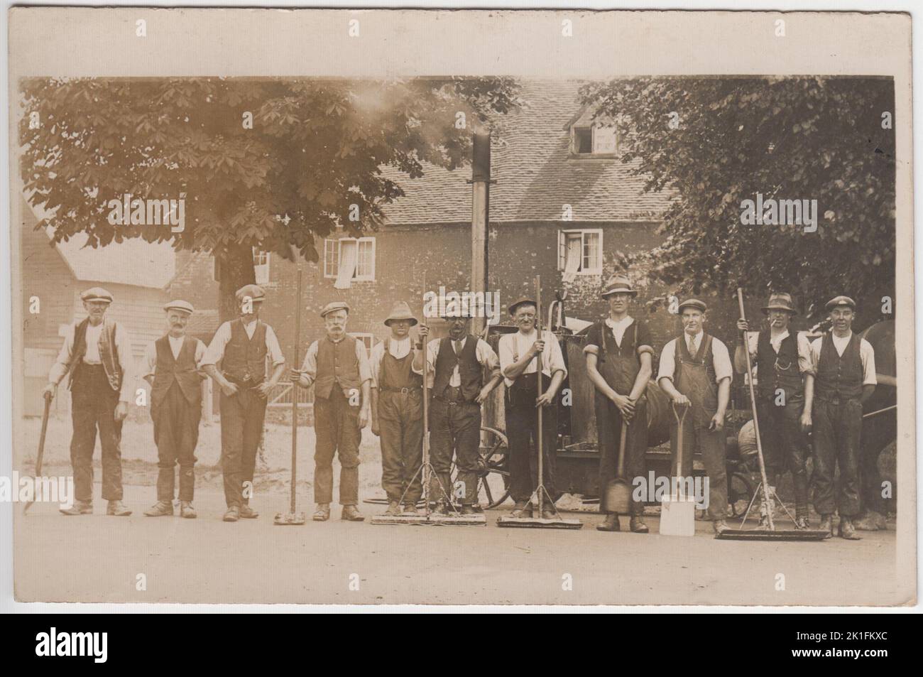Les fauteurs de route du début du 20th siècle photographiés dans des vêtements de travail, tenant des bêches et des brosses. Ils sont photographiés devant une machine à vapeur tirée par des chevaux Banque D'Images