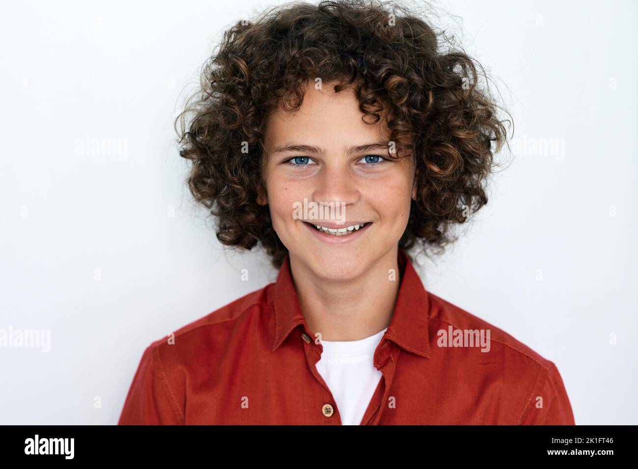 Portrait d'un beau garçon aux cheveux bouclés avec un sourire crasseux et des yeux bleus, isolé sur fond blanc Banque D'Images