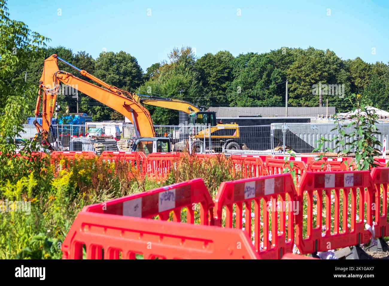 Grue de route jaune sur un chantier de construction en gravier avec un ciel bleu et des arbres verts en arrière-plan Banque D'Images