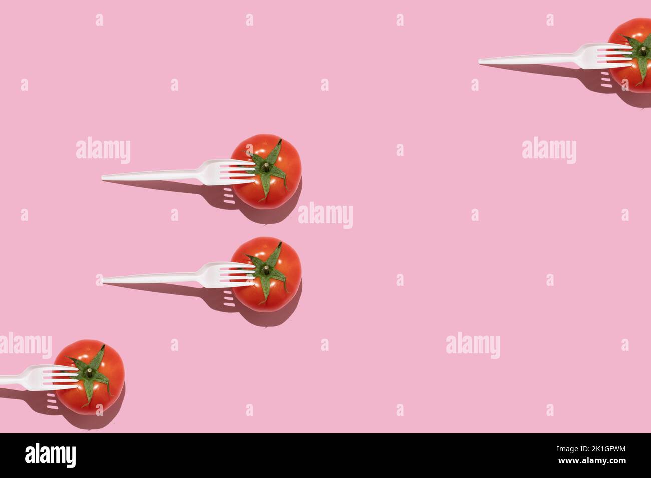 Concept alimentaire créatif. Tomates fraîches avec des fourchettes en plastique blanc sur fond rose. Banque D'Images