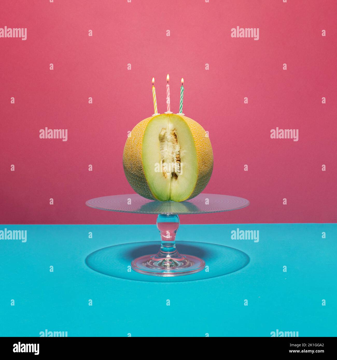 Melon frais avec trois bougies d'anniversaire sur gâteau de verre stand sur fond rose et bleu. Concept minimal. Banque D'Images