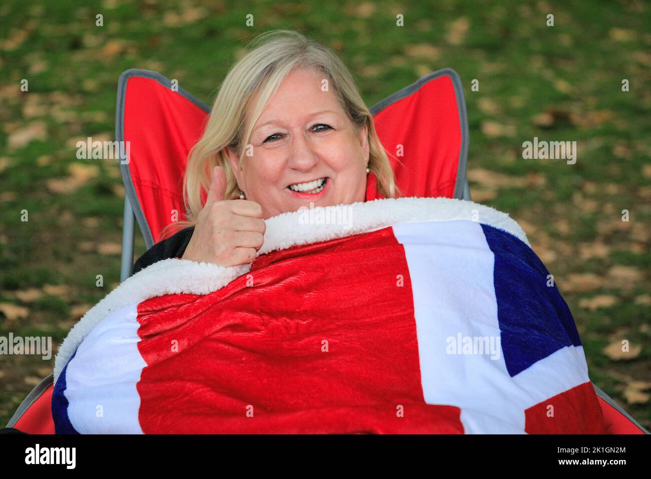 Londres, Royaume-Uni. 18th septembre 2022. Une femme sourit dans son sac de couchage Union Jack. Les membres de la file d'attente publique attendent le long de la route pour les funérailles de la reine Elizabeth II sur le Mall à Westminster. Beaucoup ont apporté des couvertures, des drapeaux de jack d'Union, des sacs de couchage, des chaises, des ballons et même des tentes crédit: Imagetraceur/Alamy Live News Banque D'Images