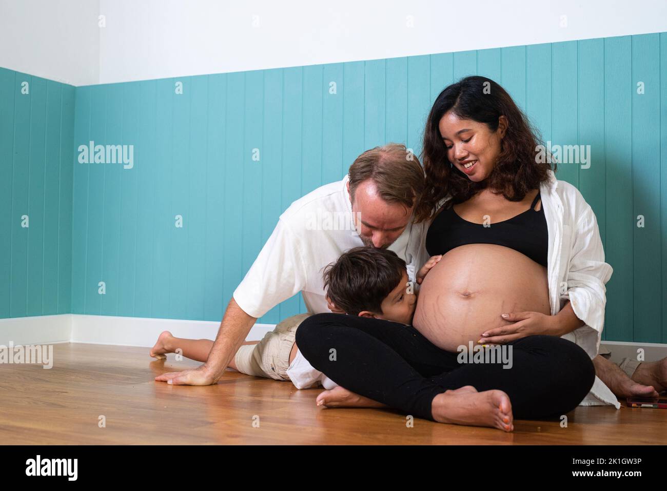 Photo de jeune couple gai positif souriant femme enceinte et mari avec leur fils à la maison Banque D'Images