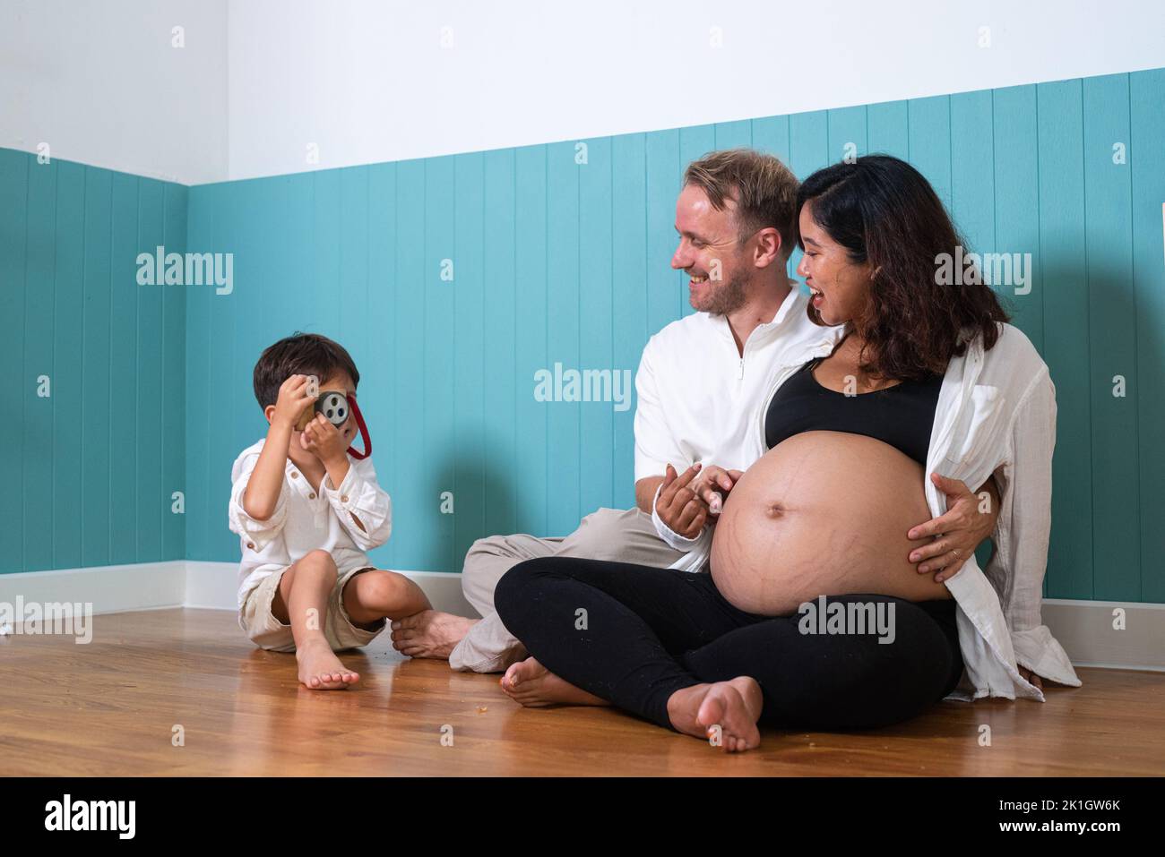 Photo de jeune couple gai positif souriant femme enceinte et mari avec leur fils à la maison Banque D'Images