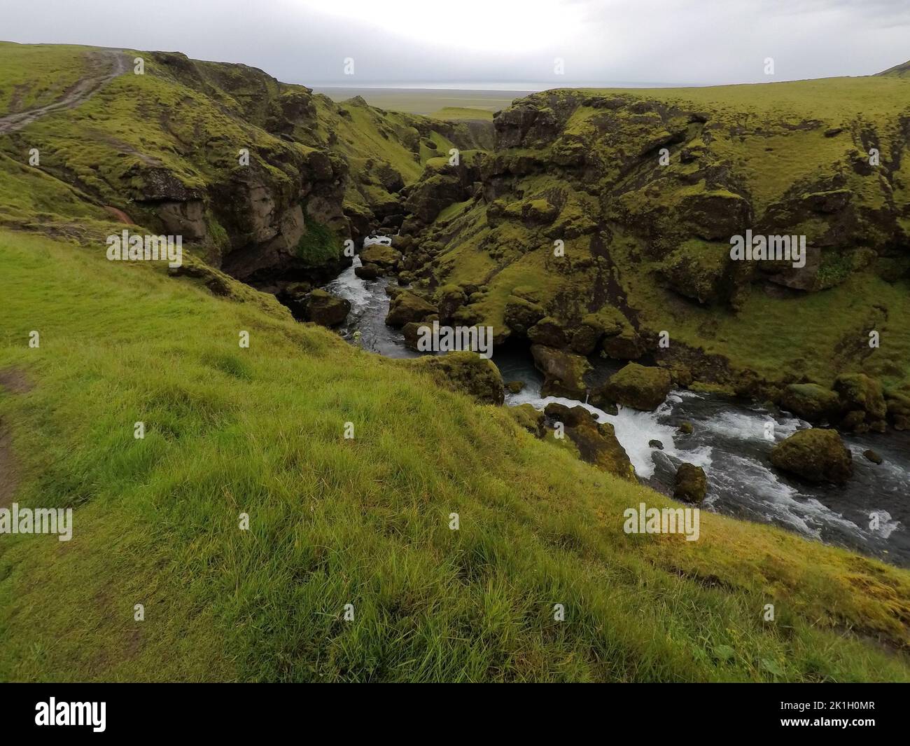Une vue panoramique d'une cascade qui coule entre les falaises d'herbe sous un ciel gris Banque D'Images
