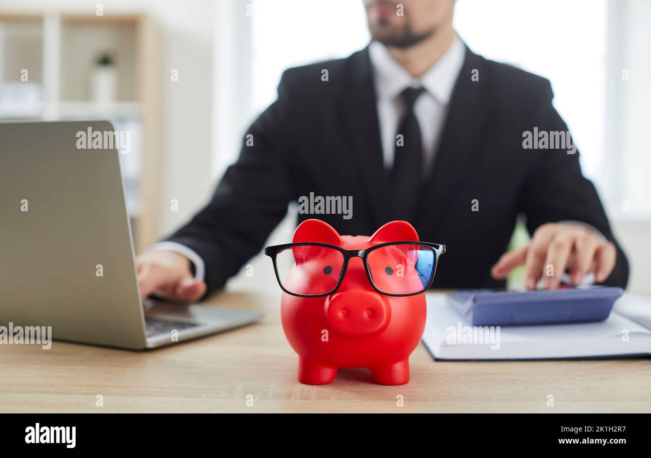 Gros plan de la banque de porc rouge sous forme de supports de porc sur la table contre le financier mâle. Banque D'Images