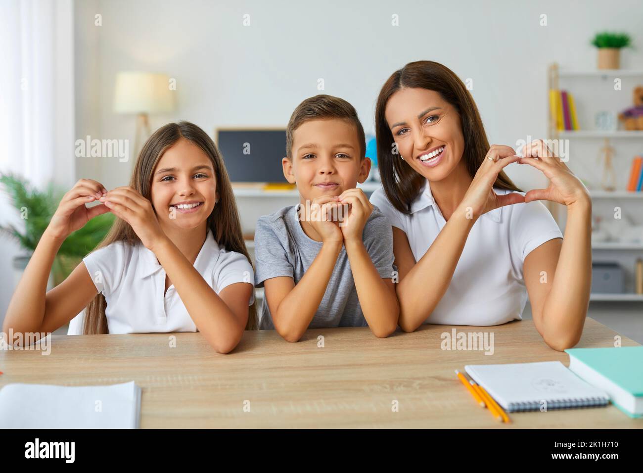 Les enfants et les femmes caucasiens heureux montrent le coeur geste assis dans le bureau d'école Banque D'Images