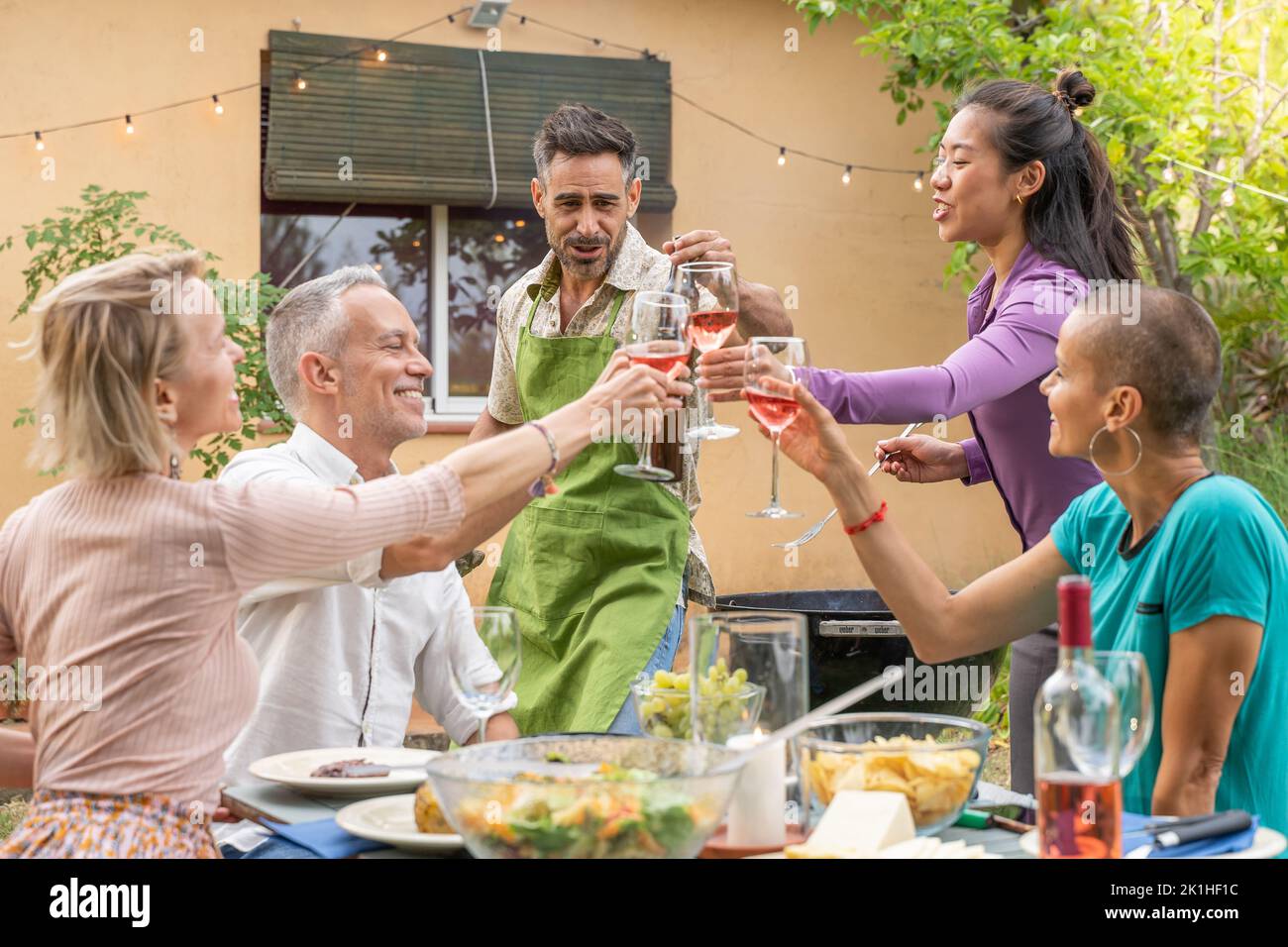 Des amis qui se coutent avec un grand sourire autour de la table au patio de la maison. Banque D'Images