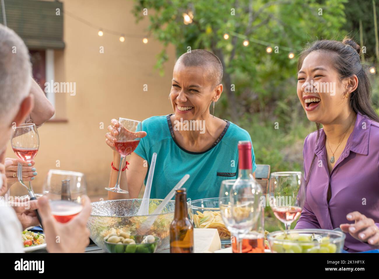 Amis multiraciaux manger et boire heureux sourire et rire dans le patio. Personnes d'âge moyen et gaies autour de la table. Banque D'Images