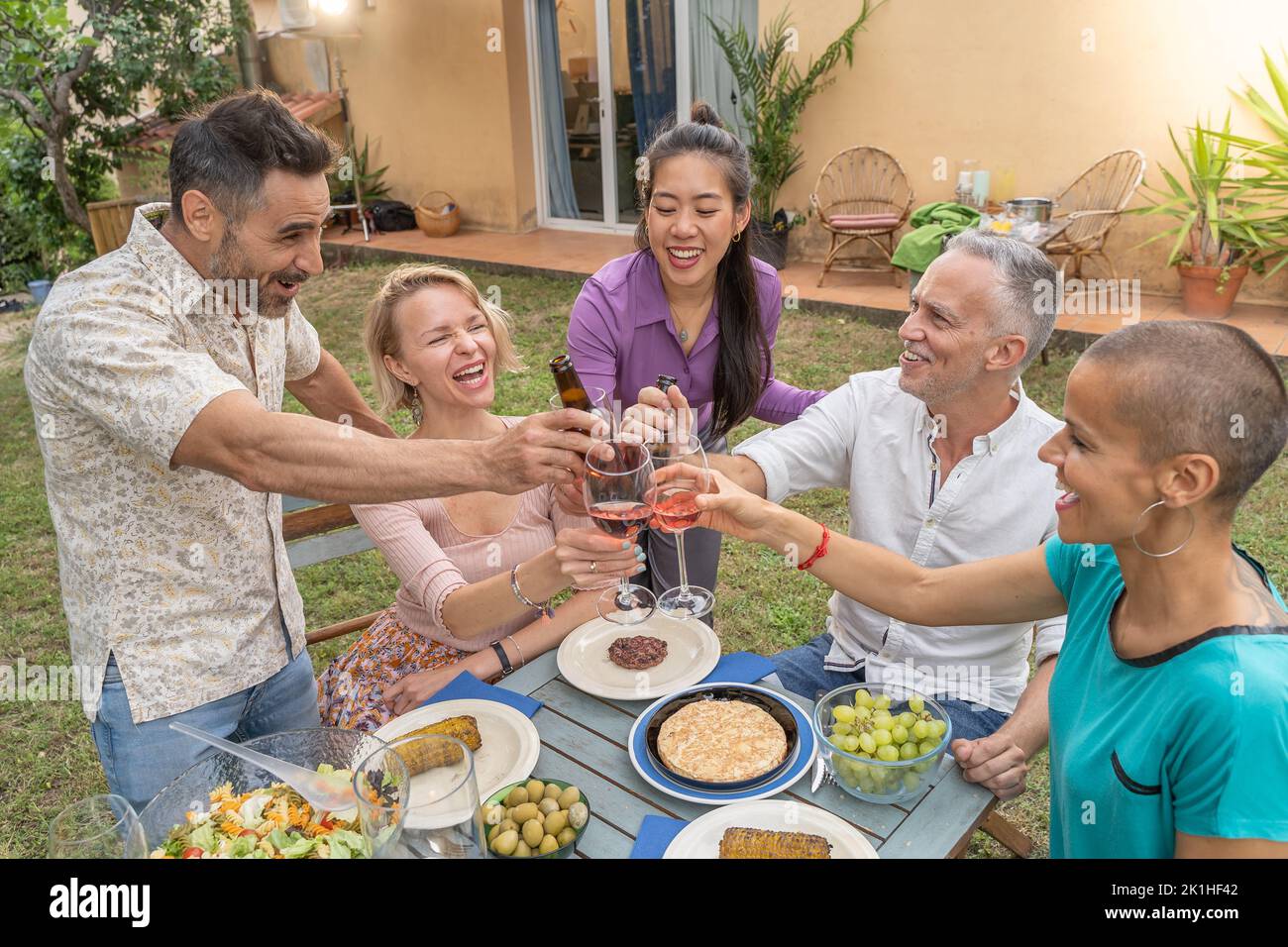 Des amis multiraciaux dégustent et dégustent du vin autour de la table au restaurant sur le patio de la maison. Banque D'Images