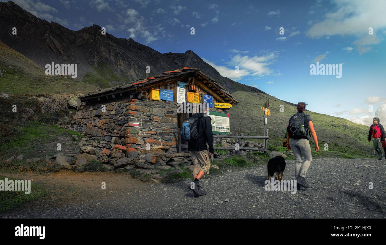 Un groupe de randonneurs avec un chien passant par un petit chalet en briques dans les montagnes avec une montagne en arrière-plan Banque D'Images