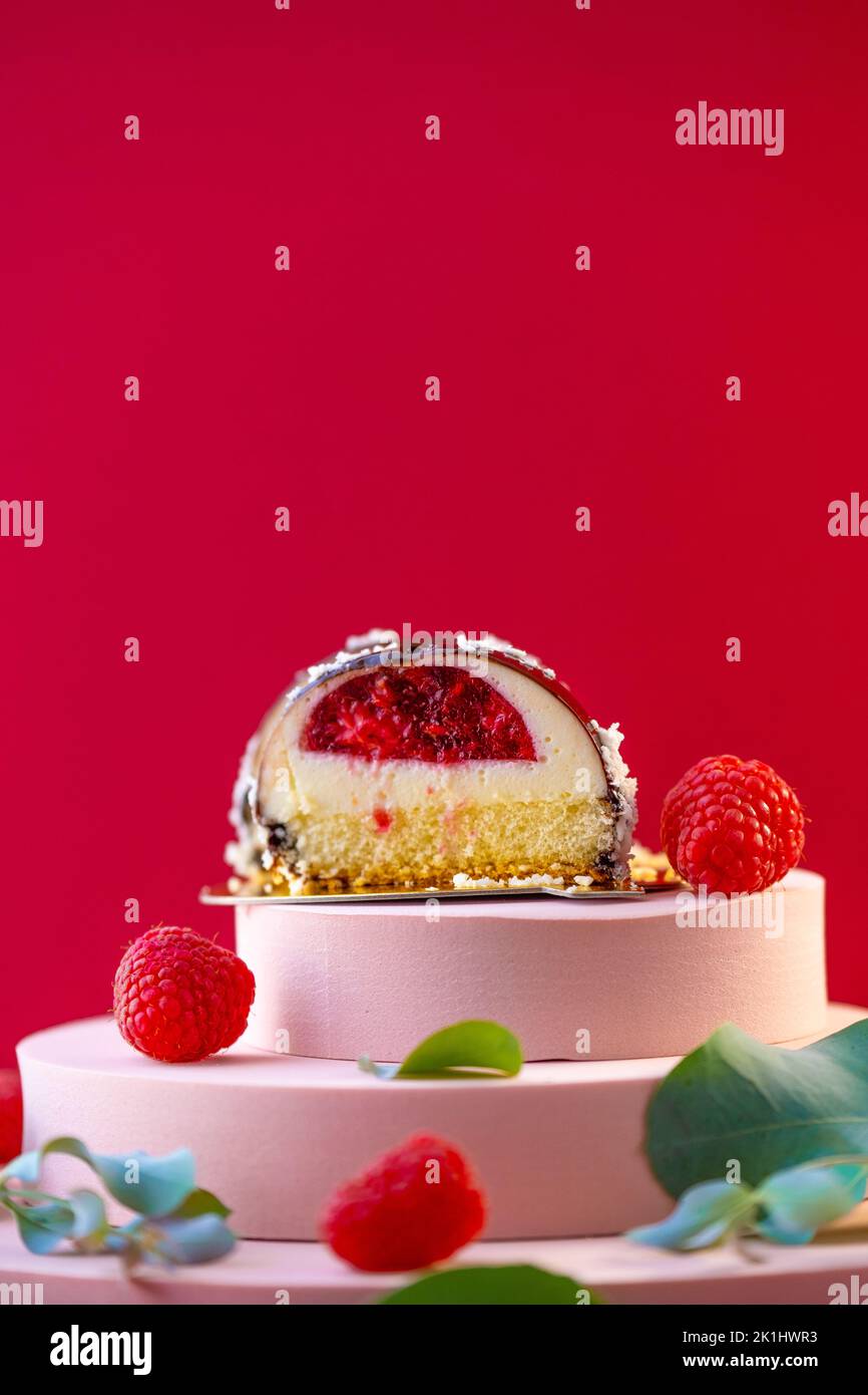 Gâteau à la coupe de framboise et framboises sur un podium rose sur fond rouge.délicat gâteau aéré soufflé.Choux pâtisserie. Banque D'Images