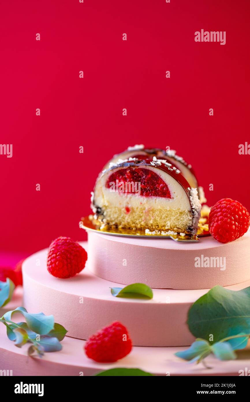 Gâteau aux baies avec coupe de framboise et framboises sur un podium rose sur fond rouge vif. Soufflé délicat et aéré Banque D'Images