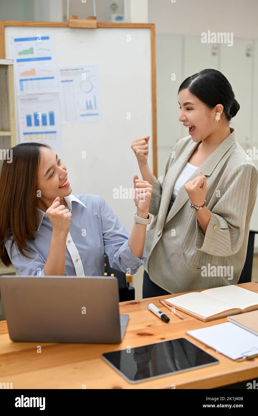 Portrait, deux femmes d'affaires asiatiques millénaires heureuses et surjoyeuses célèbrent leur succès ensemble dans le bureau. La victoire de la victoire de la victoire, la réalisation de but toge Banque D'Images