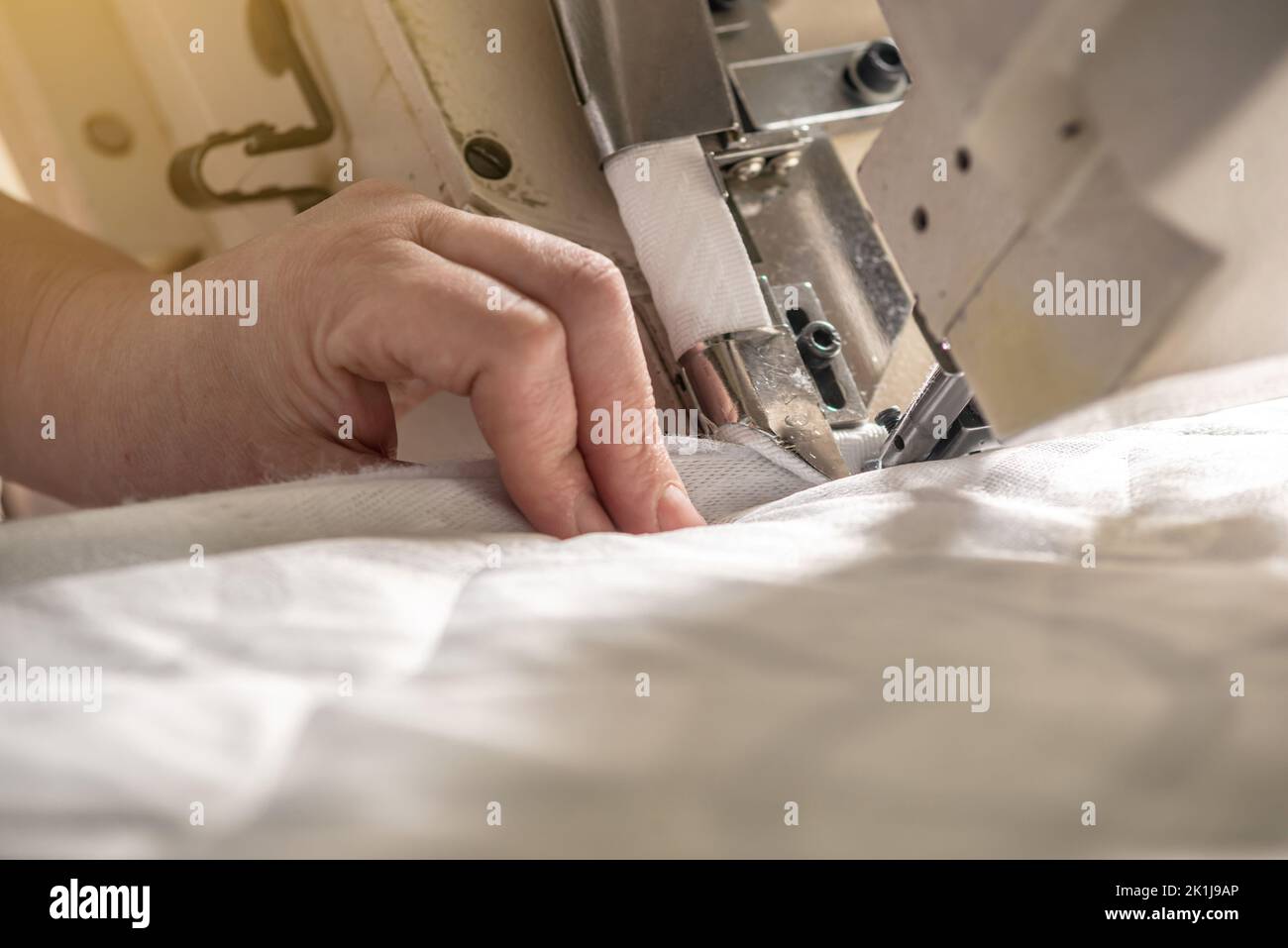 Les mains des femmes dans le processus de couture sur l'équipement professionnel. Couture de tissus en production. Gros plan. Banque D'Images
