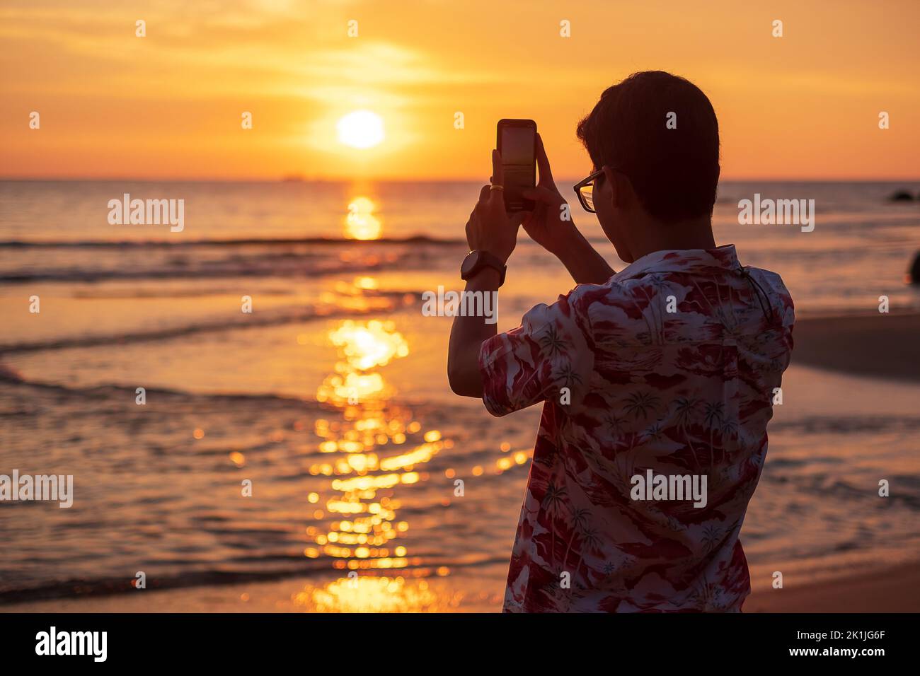 Silhouette de jeune homme heureux prenant des photos par smartphone.Tourist Profitez du beau coucher de soleil sur la plage. Voyage, détente, vacances concept été Banque D'Images