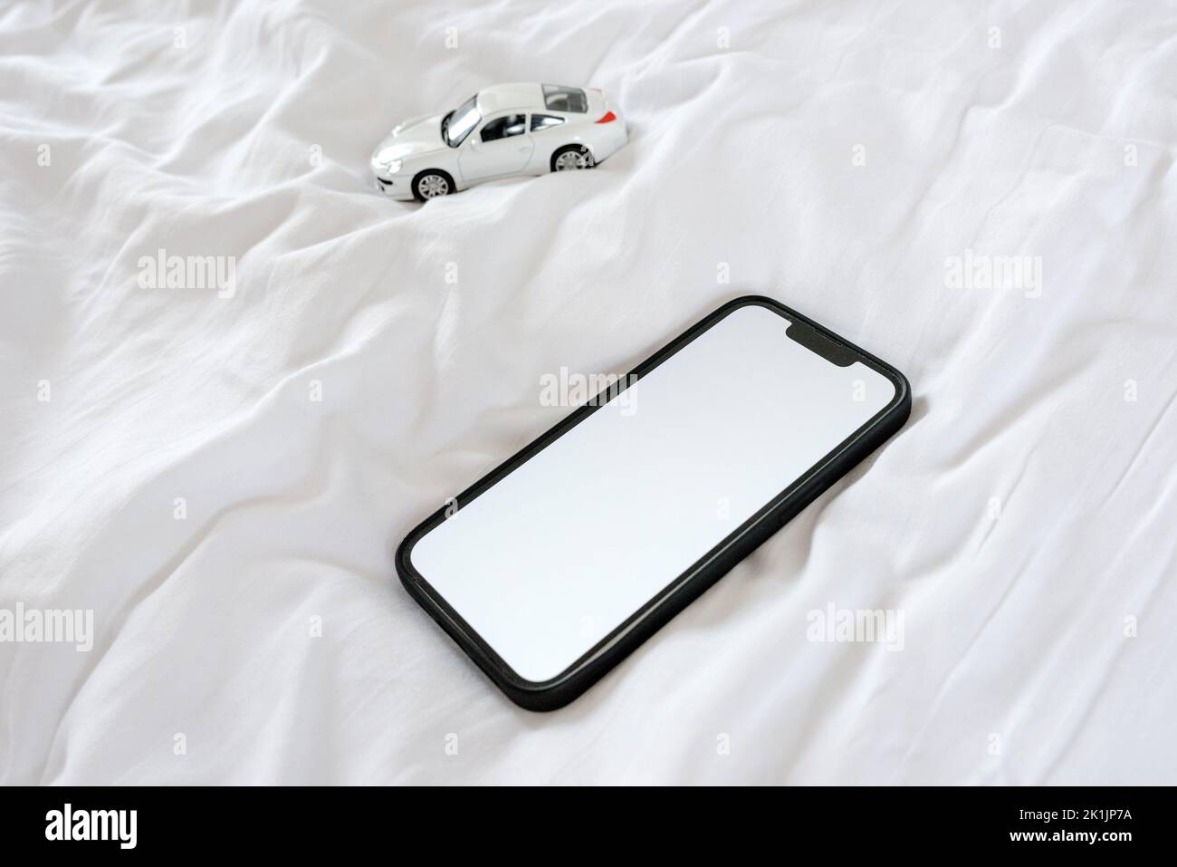 Smartphone et voiture modèle moulée sur le lit. Téléphone portable avec écran de maquette blanc vierge comme espace de copie. Mise au point sélective. Banque D'Images