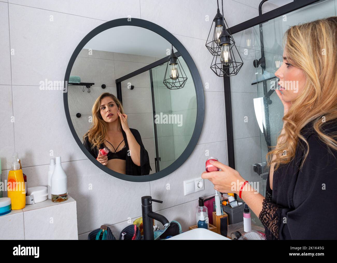 jeune fille blonde faisant son maquillage devant le miroir en lingerie noire Banque D'Images