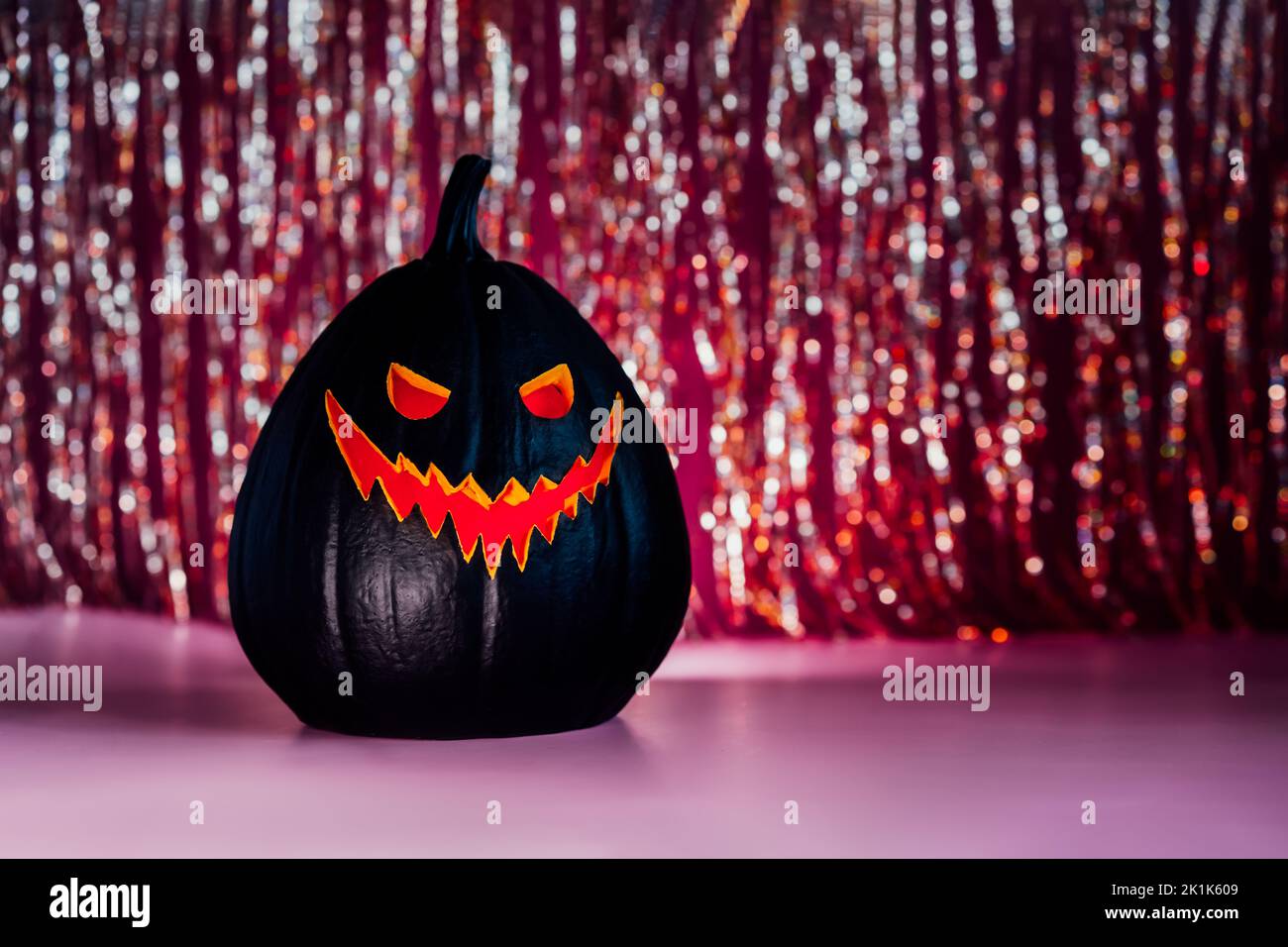Citrouille noire d'halloween effrayante, lanterne Jack O, avec le visage et les yeux mal illuminés rouges sur le rideau scintillant sur le fond. Joyeux Halloween d Banque D'Images Citrouille noire d'halloween effrayante, lanterne Jack O, avec le visage et les yeux mal illuminés rouges sur le rideau scintillant sur le fond. Joyeux Halloween d Banque D'Images