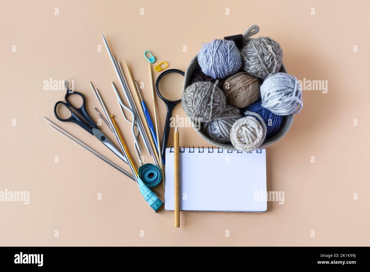 Accessoires de tricotage, crochet, aiguilles, ciseaux, loupe, centimètre, carnet avec crayon, un panier avec des boules de fil bleu gris brun sur un Banque D'Images