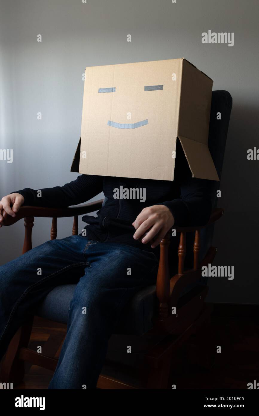 Homme souriant avec une boîte en carton sur sa tête assis dans une chaise Banque D'Images