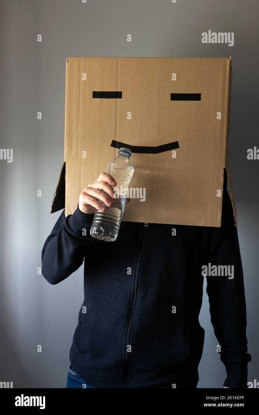 Homme souriant avec une boîte en carton sur sa tête buvant une bouteille d'eau Banque D'Images