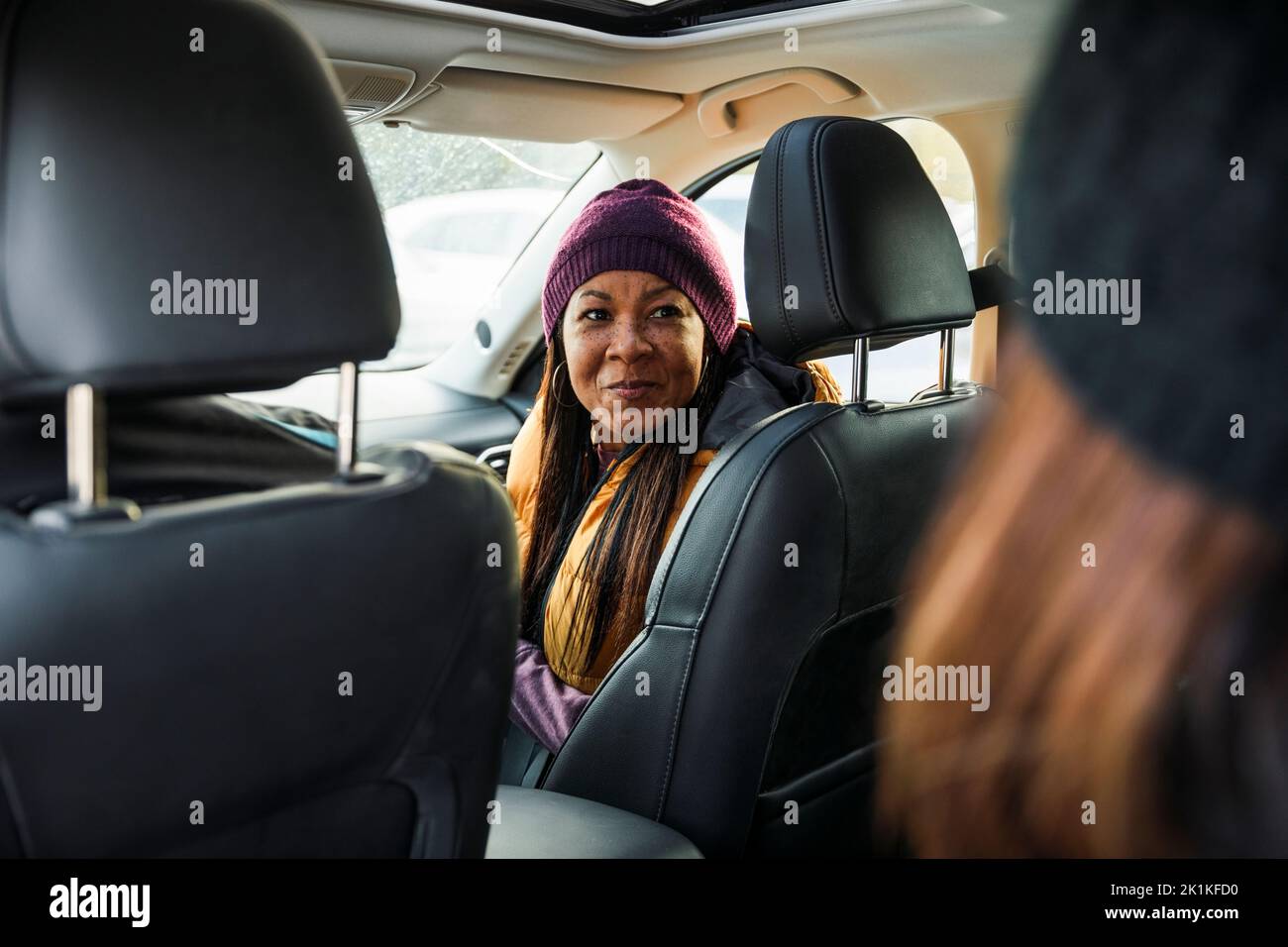 Femme assis sur le siège passager d'une voiture parlant à un ami assis à l'arrière Banque D'Images