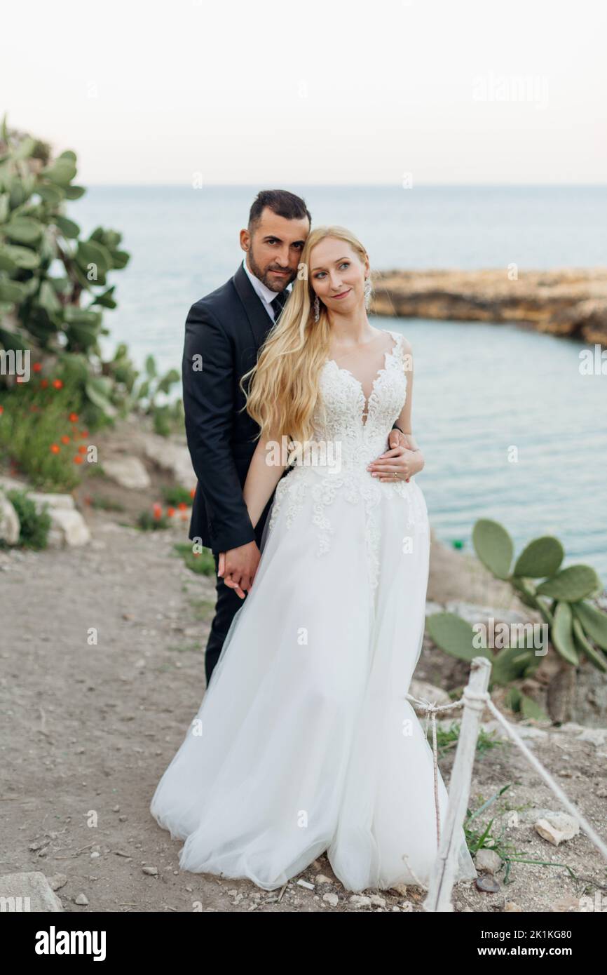 Portrait de couple de mariage debout près des feuilles de cactus d'opuntia. Jeunes mariés se marient les mains avec le marié en costume. Banque D'Images Portrait de couple de mariage debout près des feuilles de cactus d'opuntia. Jeunes mariés se marient les mains avec le marié en costume. Banque D'Images