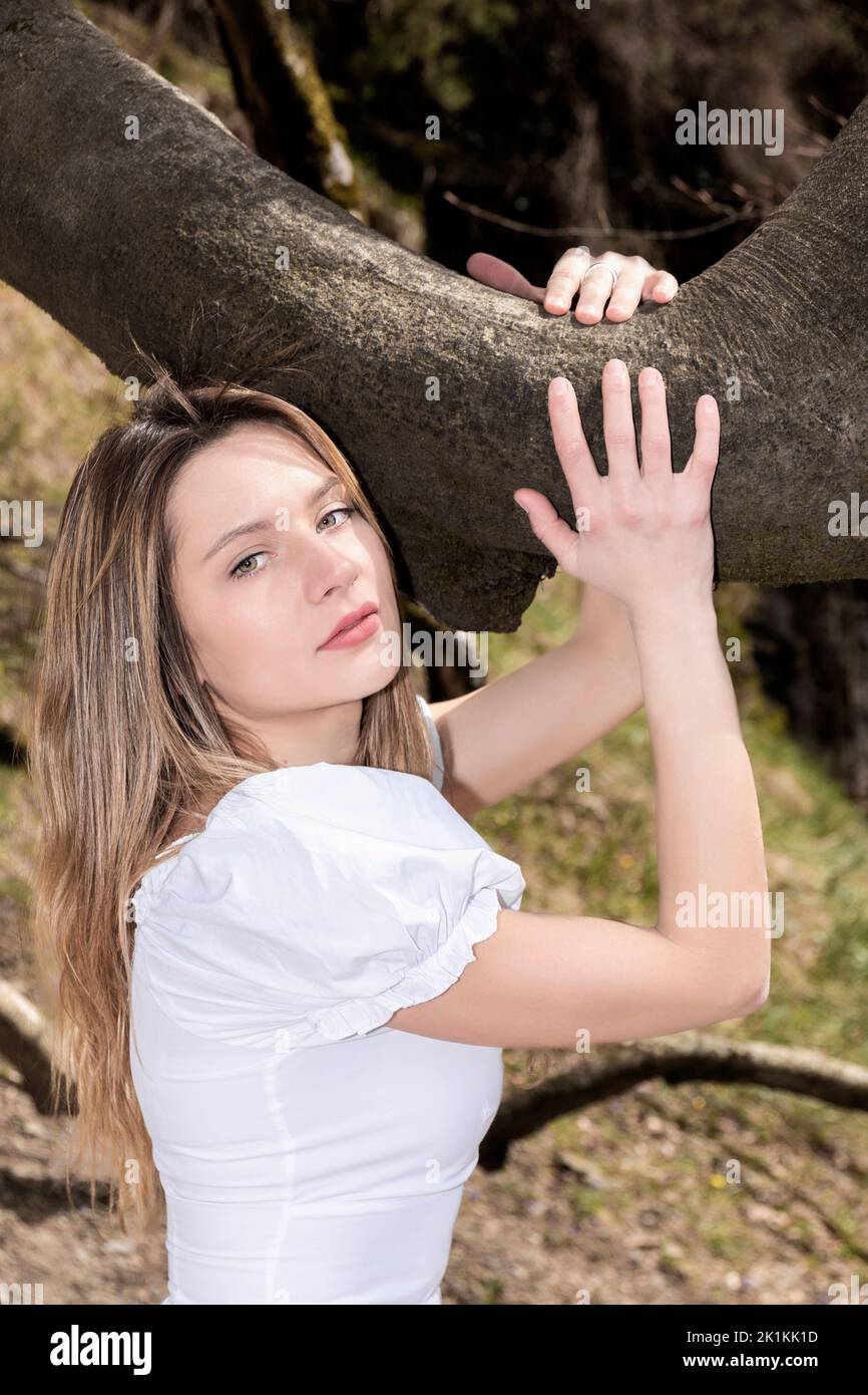 jolie femme blonde embrassant une branche d'arbre dans une robe blanche Banque D'Images