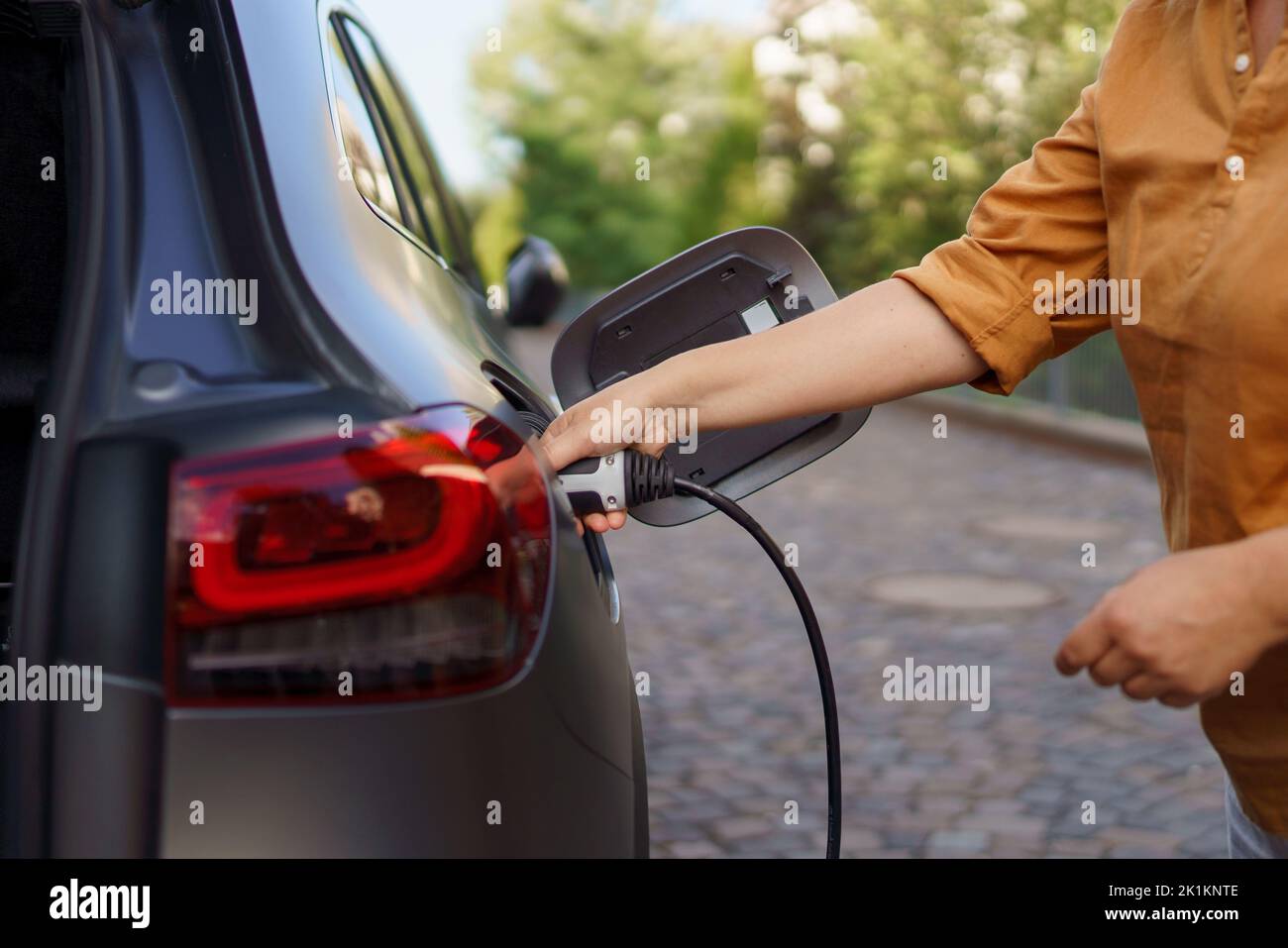 Femme tenant le câble d'alimentation électrique à la station de charge du véhicule électrique, à proximité Banque D'Images