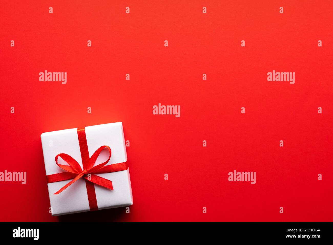 Carte postale créative de Noël et de la Saint-Valentin avec boîte cadeau blanche et noeud en ruban rouge sur fond de papier rouge. Concept Saint-Valentin et amour Banque D'Images