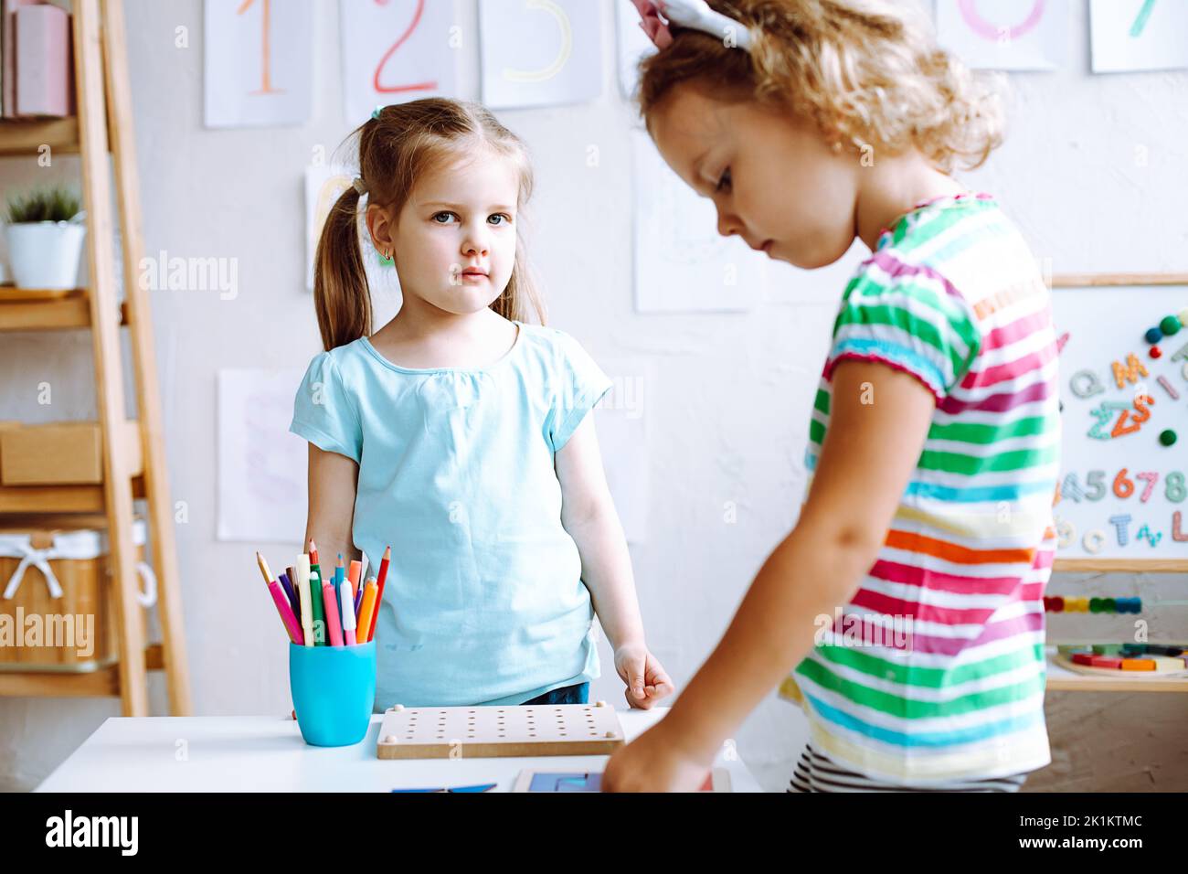 Jolies petites filles qui étudient et jouent avec des jouets sur le bureau dans la salle de jeux de près. Leçon intéressante pour les jardins d'enfants de développer la logique et Banque D'Images