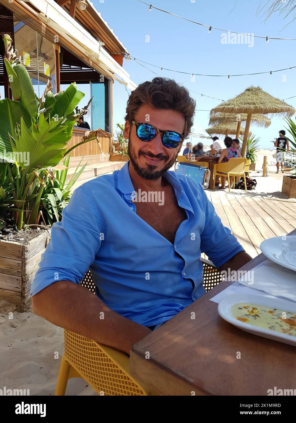 Portrait d'un homme souriant avec des lunettes de soleil, sur une terrasse de plage après le déjeuner. Banque D'Images