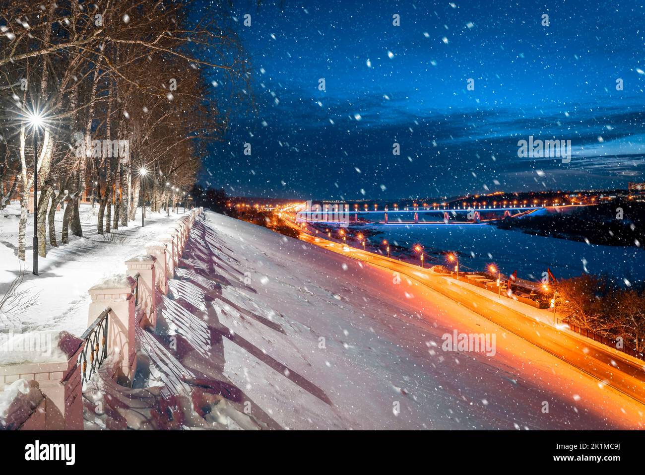 Vue de la nuit ville d'hiver couverte de neige et la route avec des traces de phares de voitures du parc de la ville. Chute de neige. Banque D'Images