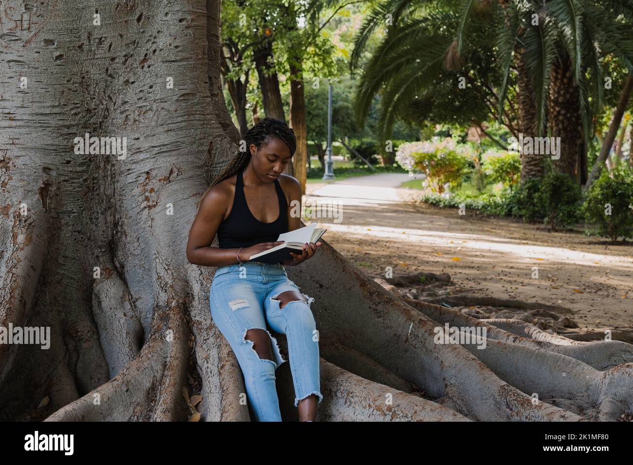 UNE JEUNE FEMME AFRO-AMÉRICAINE SE REPOSE À L'OMBRE D'UN ARBRE LISANT UN LIVRE Banque D'Images