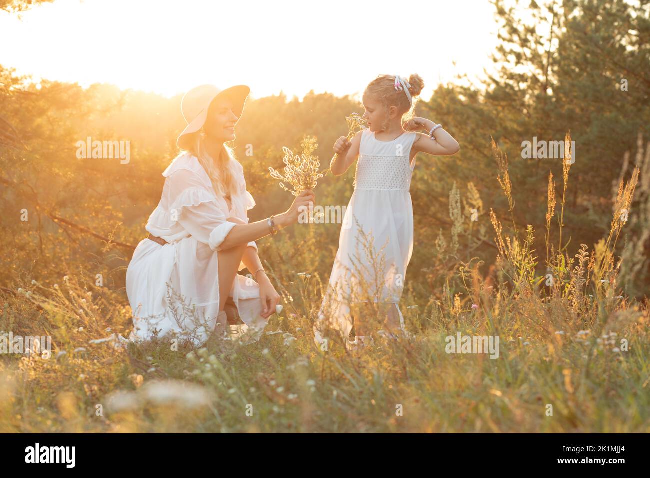 Vue latérale de la famille portant des robes blanches, debout près des pins dans la forêt illuminée par le coucher du soleil en été. Relation. Banque D'Images