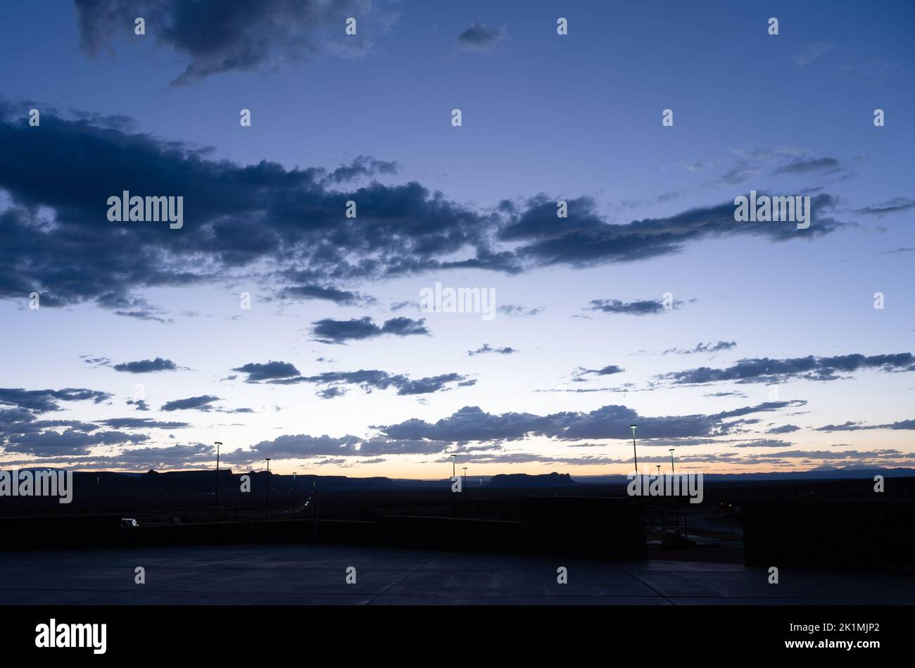 Après le coucher du soleil, le ciel brille d'un bleu profond et des bandes de nuages ombrageux se tiennent au-dessus de l'horizon sombre. Banque D'Images