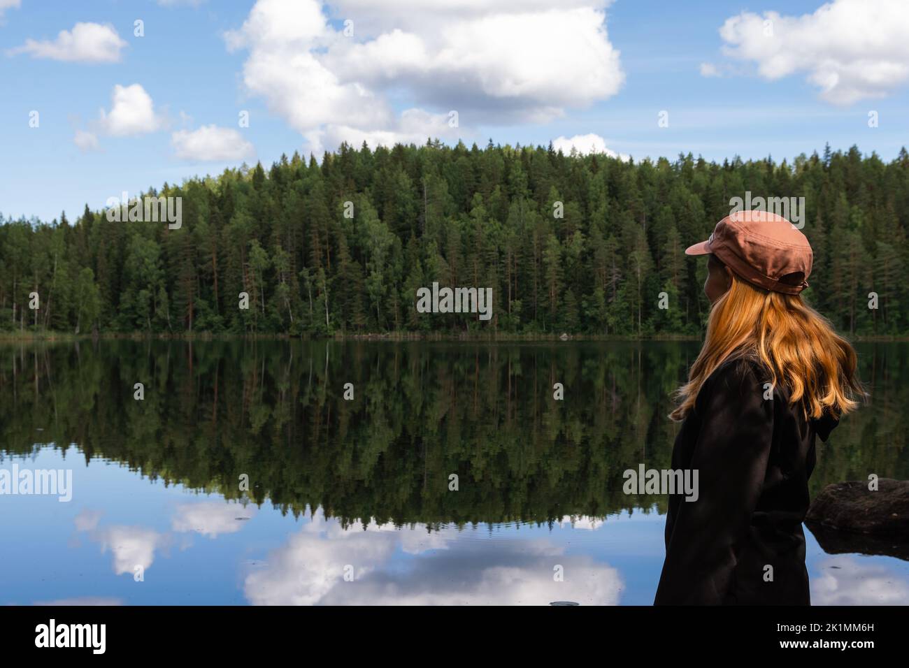 Femme aux cheveux rouges portant une casquette regardant le lac calme avec réflexion sur une belle journée d'été dans la nature Banque D'Images