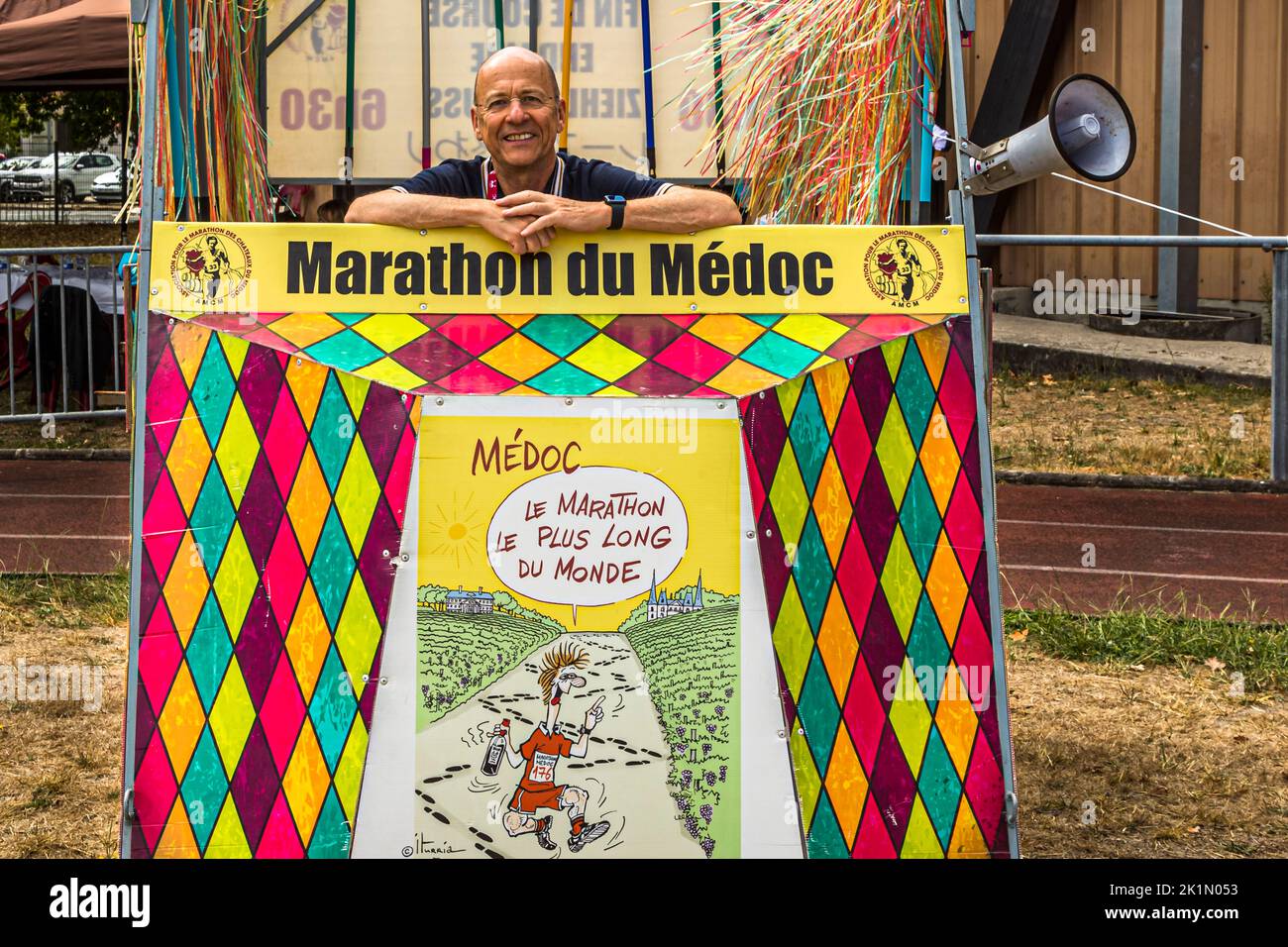 Journaliste et coureur de marathon Georg Berg se penche, riant, depuis le chariot à balais peint vif du Marathon des Châteaux du Médoc à Pauillac, en France. Une affiche de dessin animé sur le chariot promet en plaisantant "Médoc : le marathon le plus long du monde" (le marathon le plus long du monde). Le chariot à balais récupère les coureurs qui ne parviennent pas à terminer les 42,195 kilomètres dans le délai de 6,5 heures. Banque D'Images