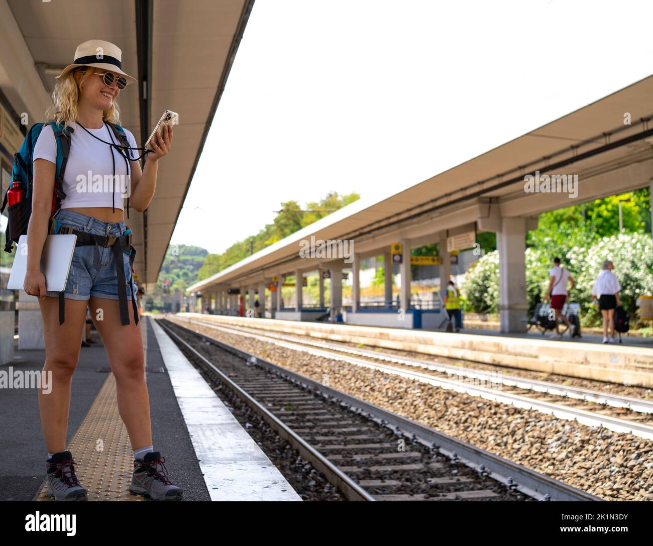 Une femme attend le train à la gare tout en travaillant volontiers sur le téléphone, le nomade numérique, le voyage et le concept de transport Banque D'Images