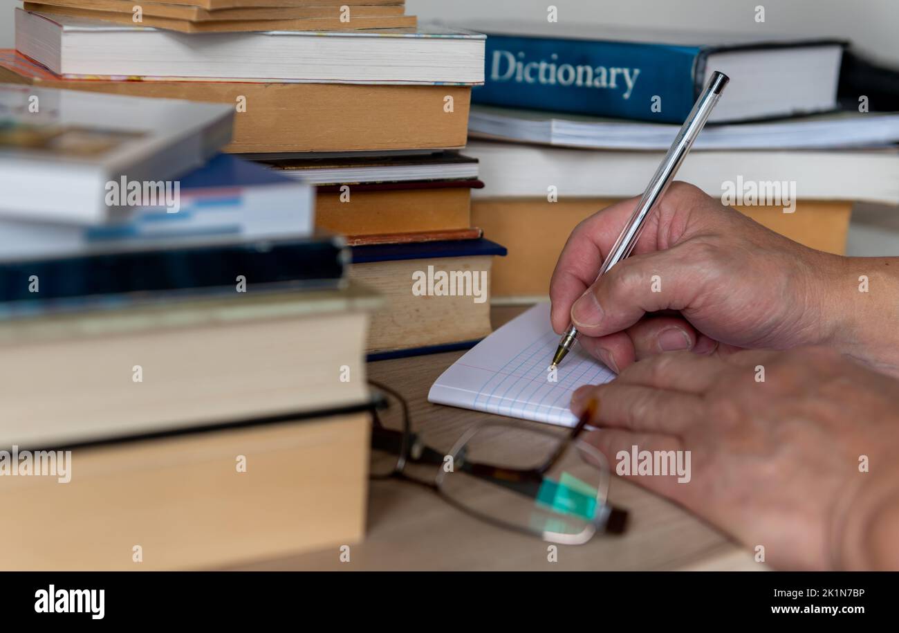 Une personne, un étudiant prenant des notes d'étude d'une pile de livres imprimés. Banque D'Images