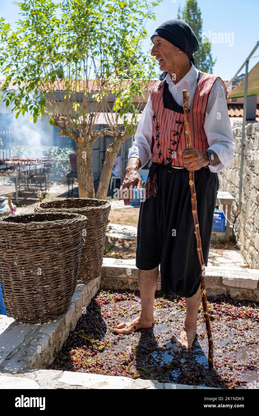 Un homme en robe traditionnelle écrasant les raisins avec ses pieds au Festival rural de Statos-Agios Fotios, région de Paphos, Chypre. Banque D'Images